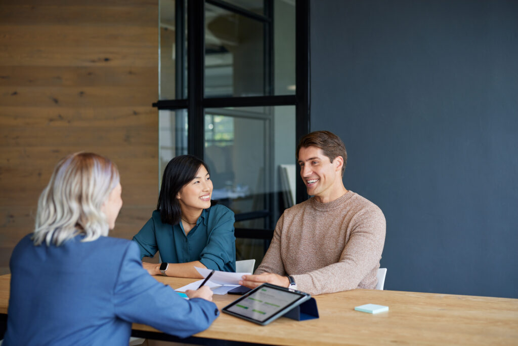 Smiling multiethnic couple receiving financial guidance from advisor with copy space. Financial agent discussing investment strategies with clients. Asian woman and his boyfriend consulting with professional for financial planning: savings and investments concept.